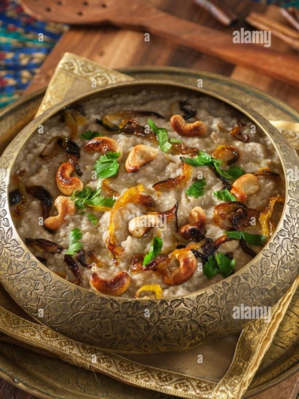 A decorative bowl filled with rich, creamy dish topped with cashews, sautéed onions, and chopped green herbs, placed on a textured golden tablecloth.